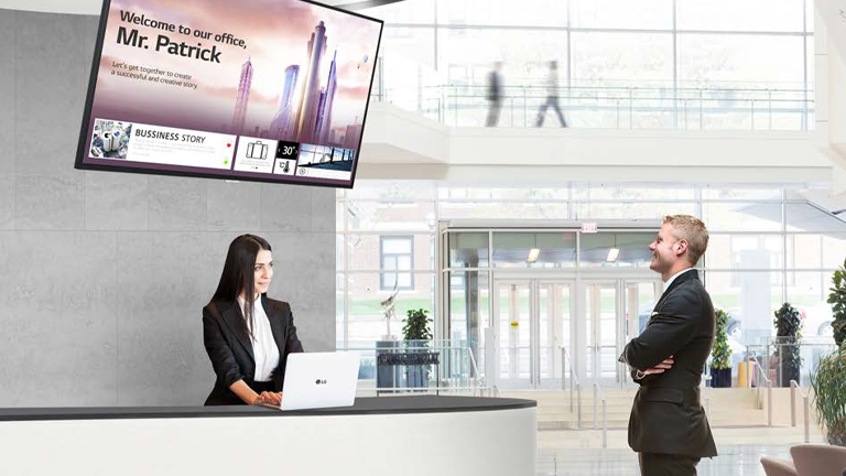 LG TV screen mounted on wall behind receptionist and a man watching LG TV